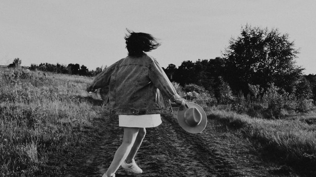 A young girl twirls joyfully outdoors on a sunny day, captured in black and white.